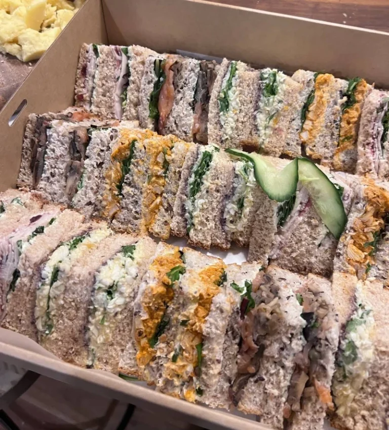 Assorted fresh sandwiches with various fillings arranged in a catering box, including vegetables, chicken, egg and tuna